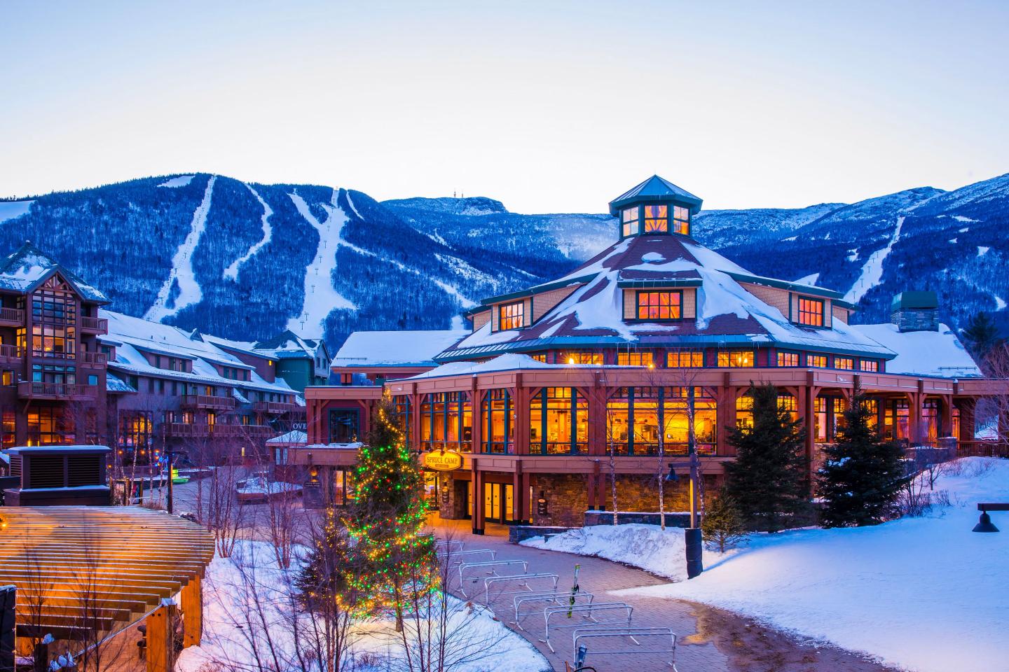 Snow-covered resort with glowing windows, mountains in the background.