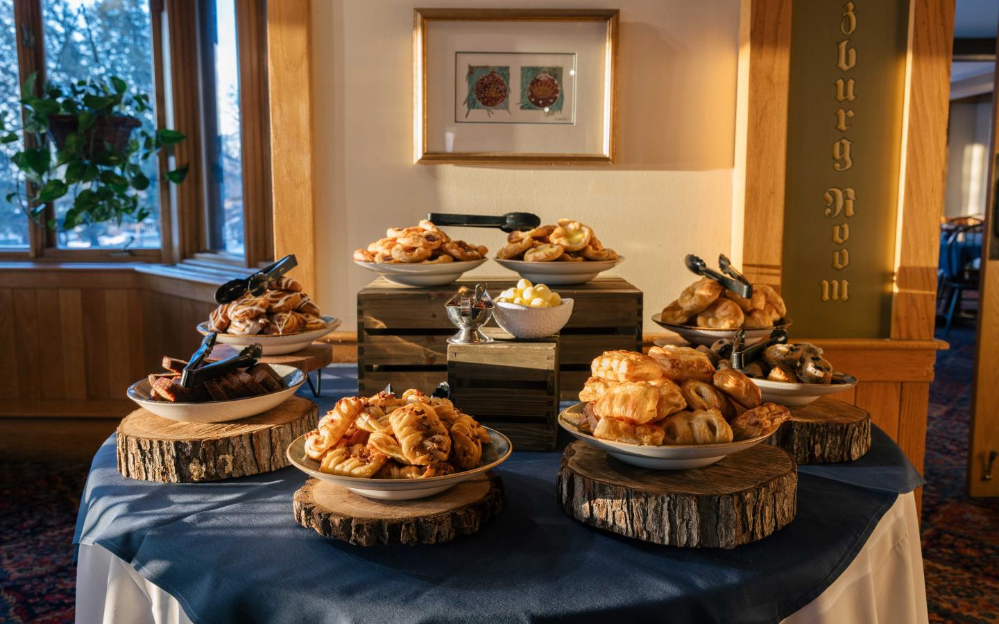 Buffet table with assorted pastries on wooden trays in a warmly lit room.