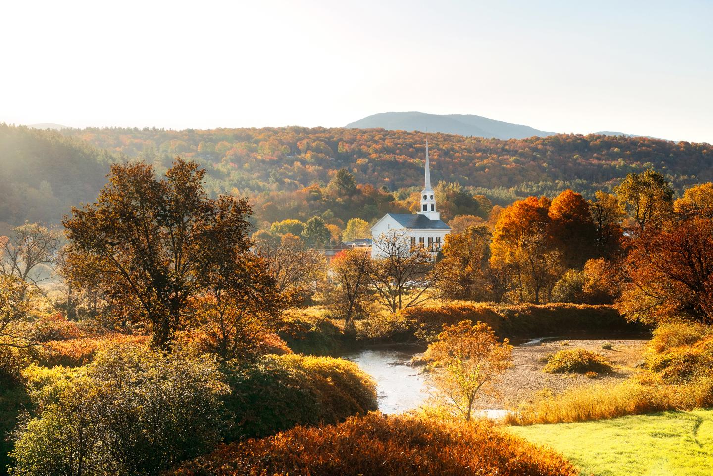 Autumn landscape in Stowe, Vermont, with a white church, colorful trees, and a small stream.
