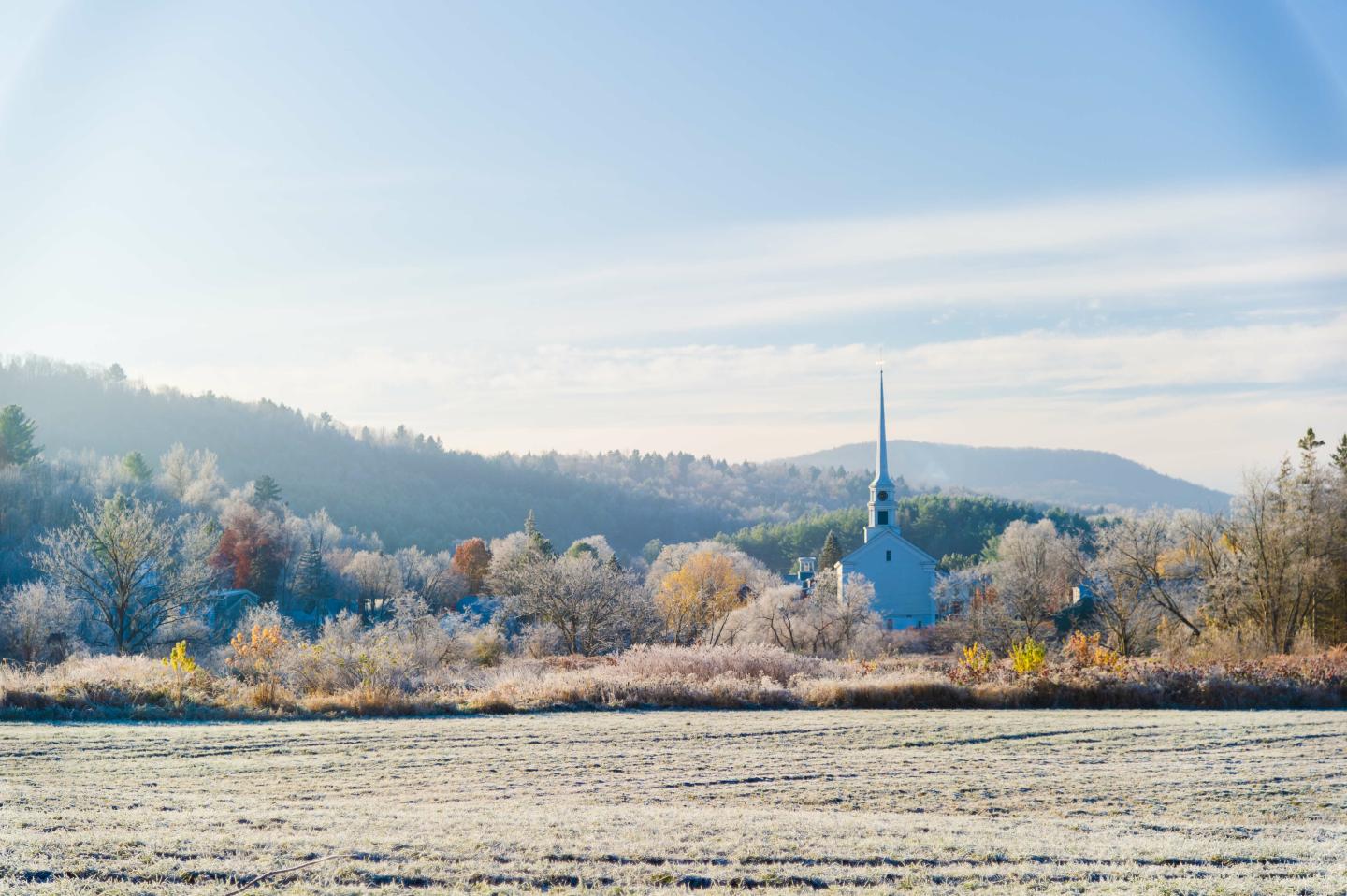 Frosty field with distant trees and church, mountains in the background.