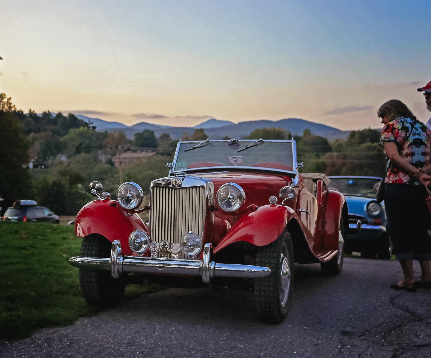 Red vintage convertible car at sunset with mountains in the background.