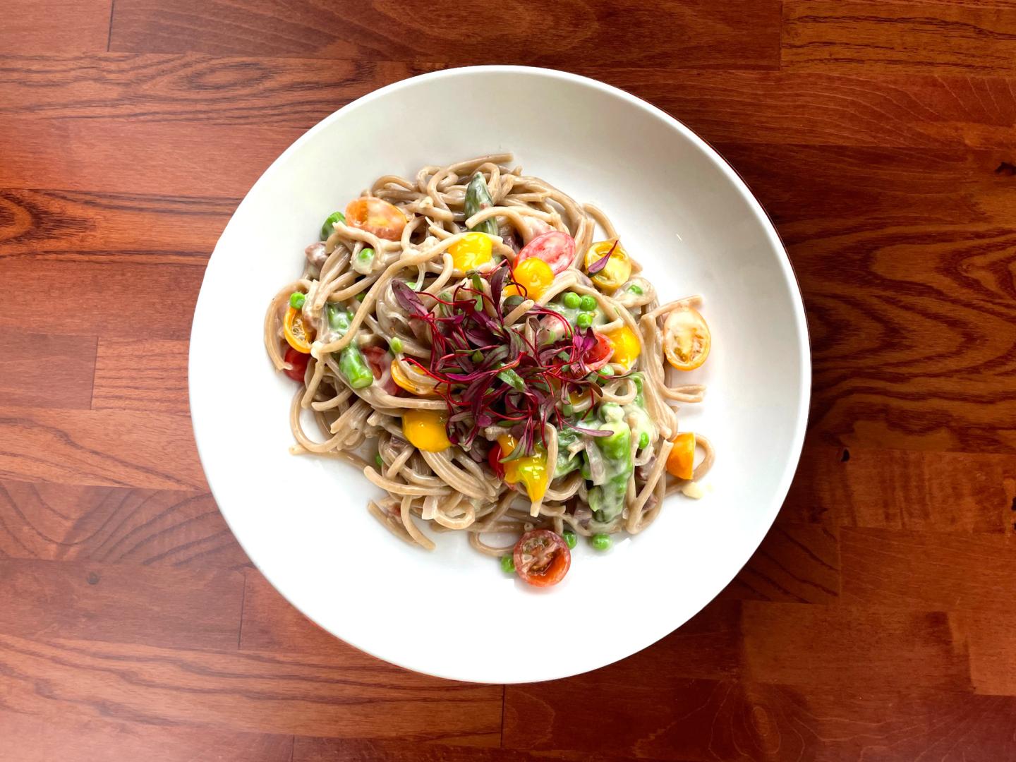 Noodles with colorful vegetables on a white plate, wooden table background.