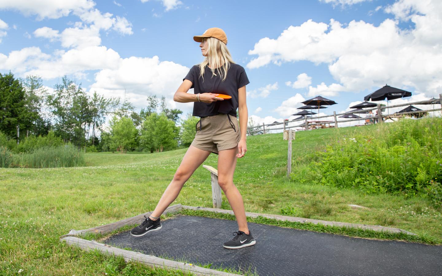 Woman playing disc golf in a grassy park under a blue sky.
