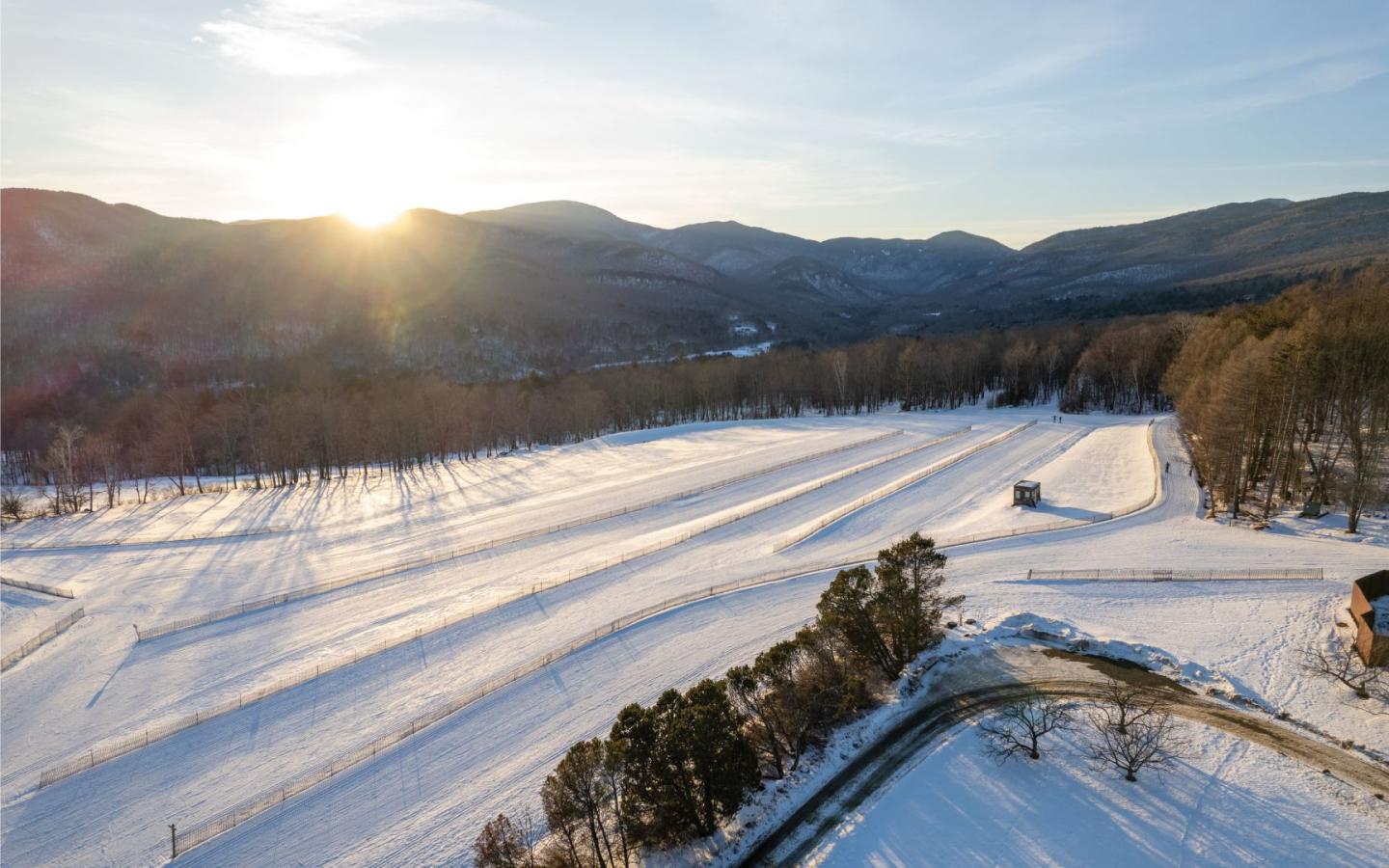 Snowy Nordic skiing trails with distant mountains at sunset.