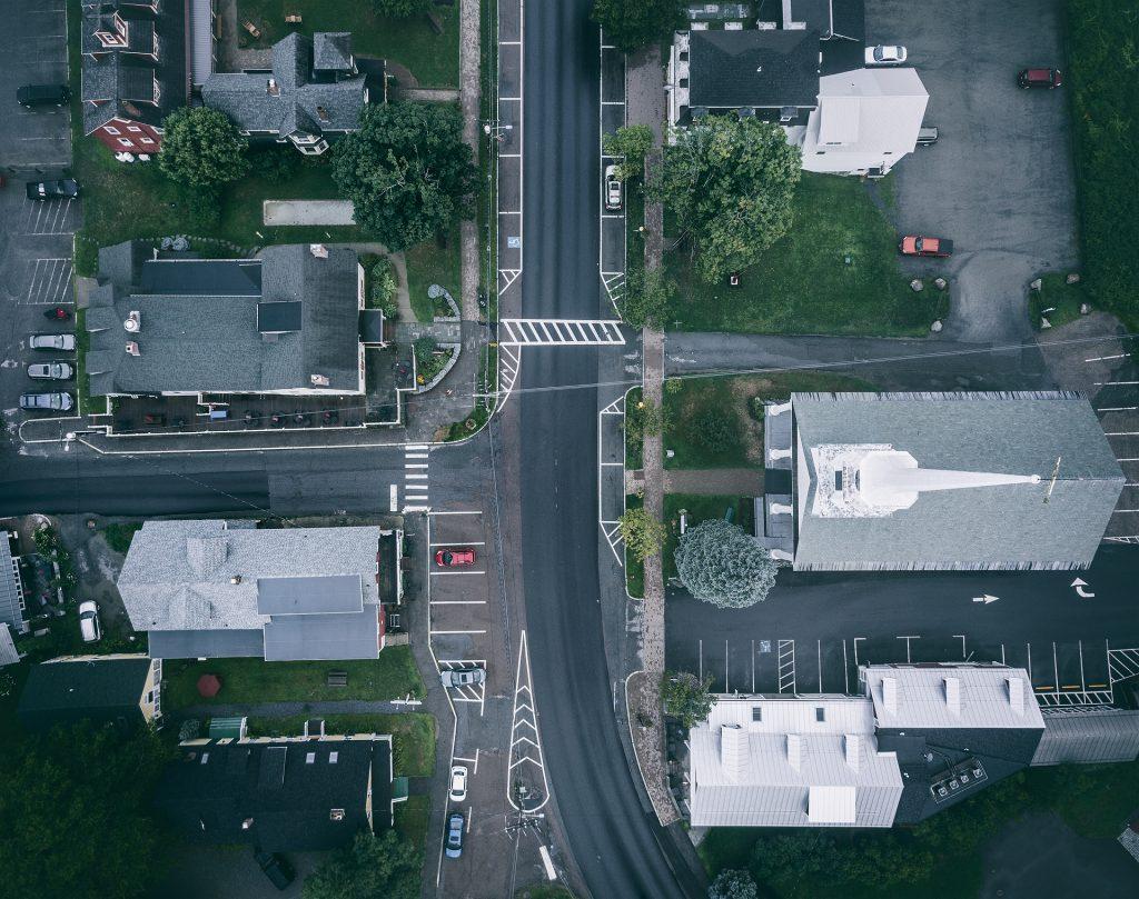 Aerial view of a small urban intersection with buildings and parked cars.