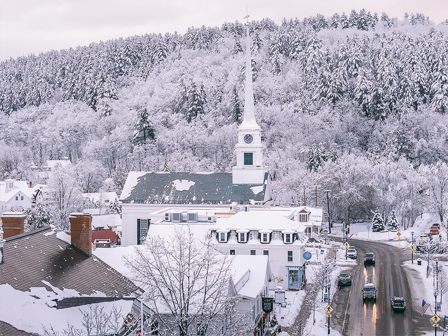 Snow-covered town with a church against a forested hillside.
