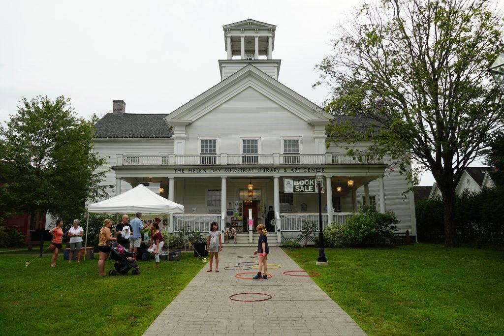 White building with cupola, people on lawn, overcast sky.