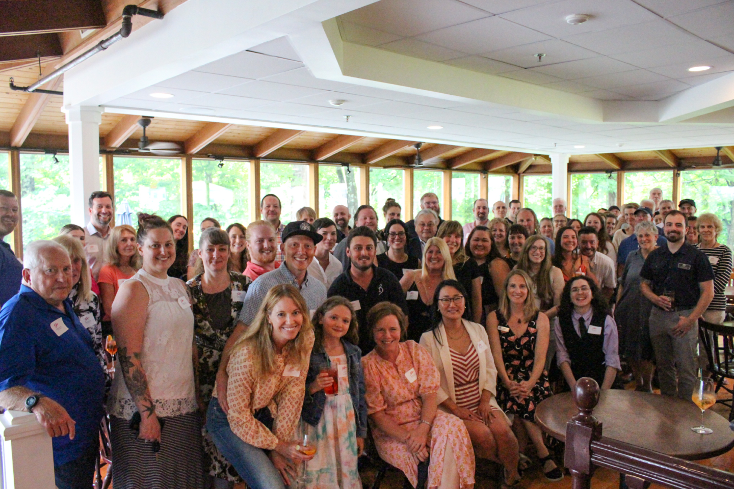 Group photo of smiling people in a sunlit room with large windows.