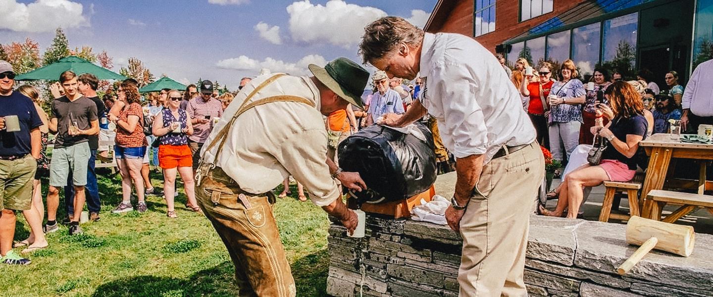 Two men tapping a beer keg outdoors at a lively gathering.