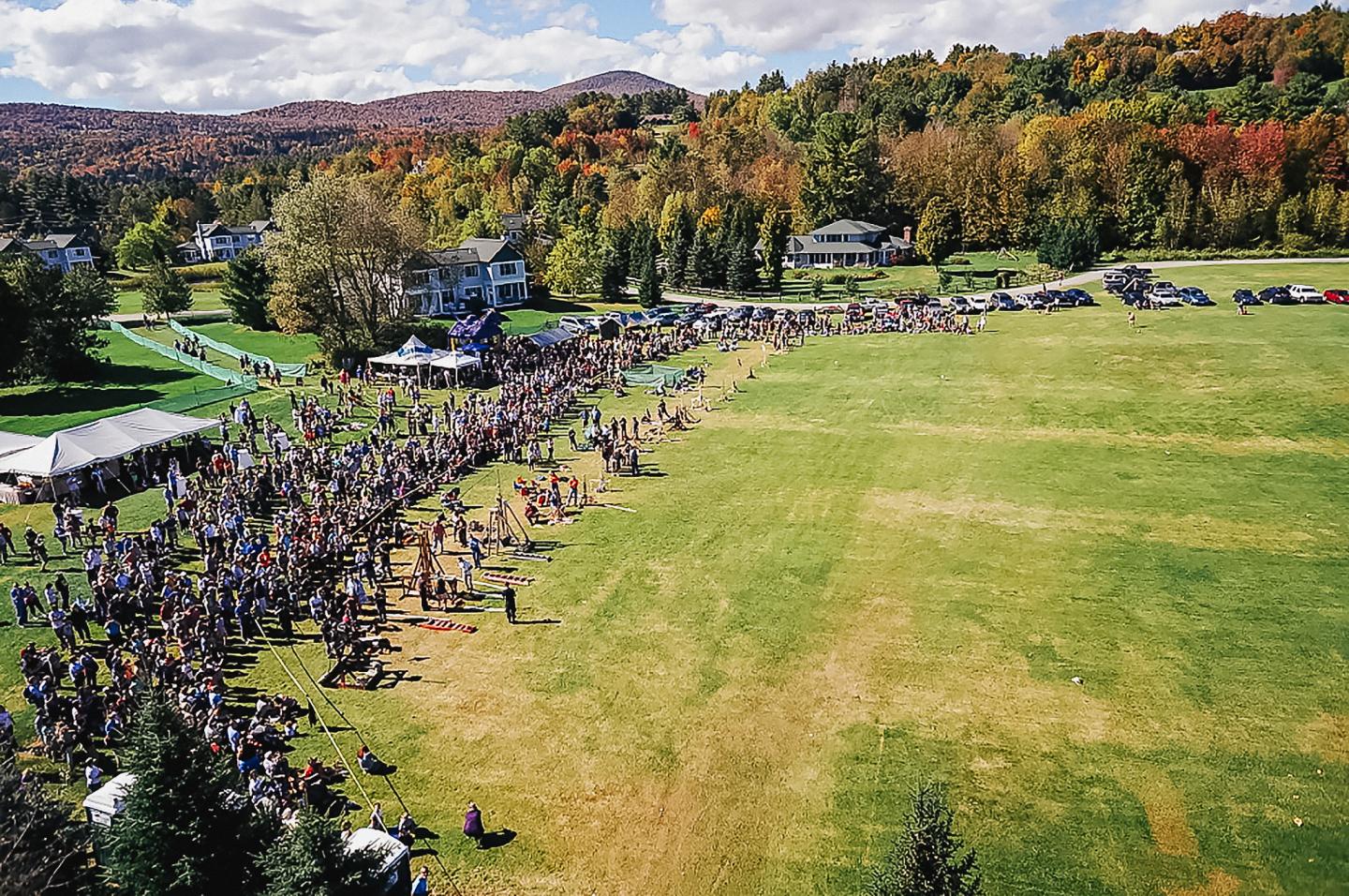 Crowd gathered on a grassy field with autumn trees in the background.