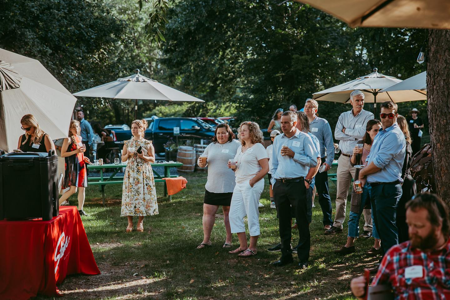 Outdoor gathering with people under umbrellas, standing and chatting.
