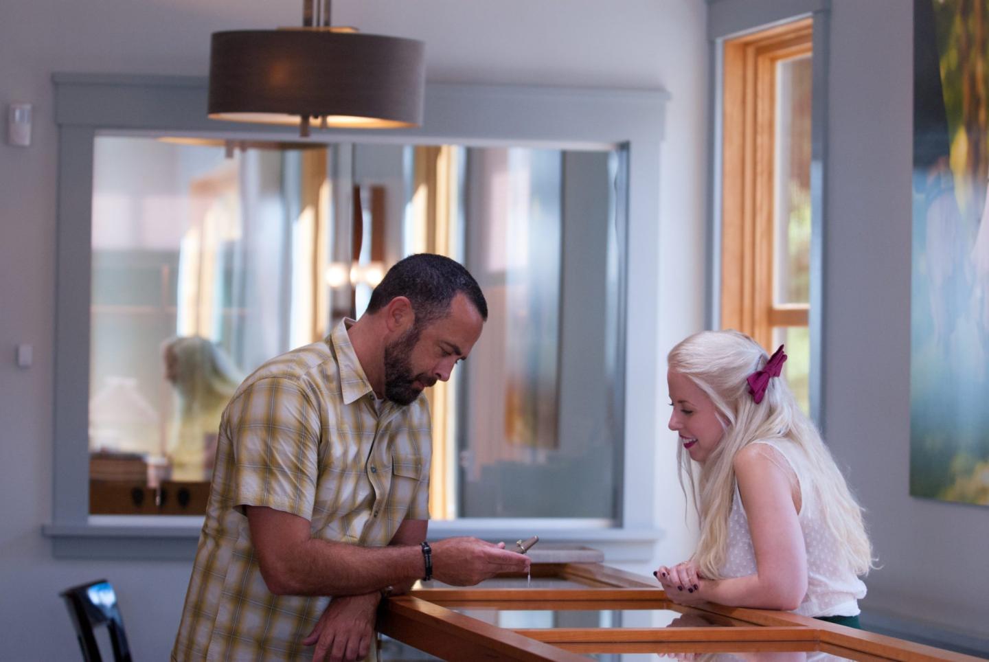 Man and woman talking at a wooden counter, bright room with large windows.