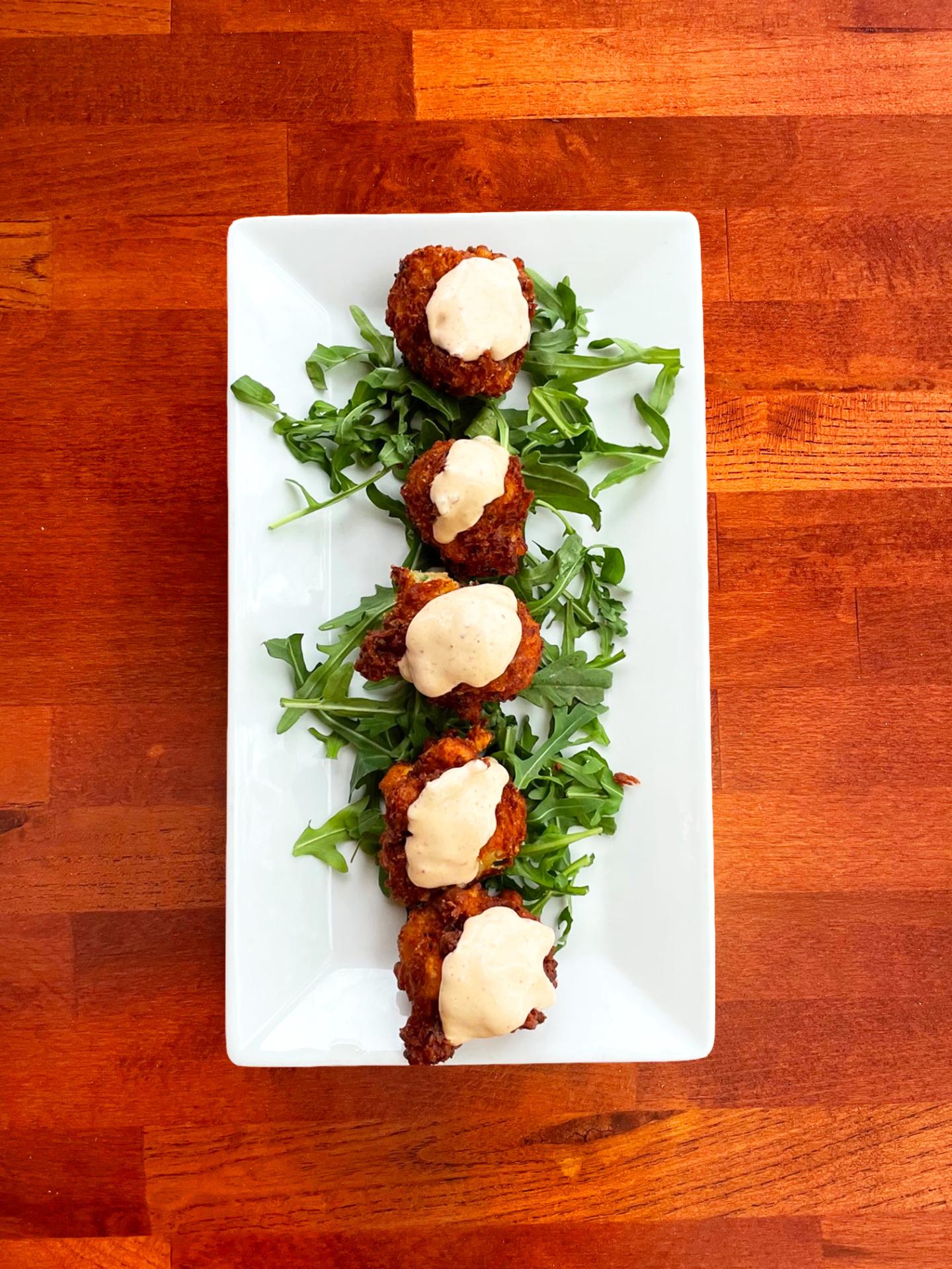 Fried Shrimp Fritters with sauce on greens, served on a rectangular white plate.