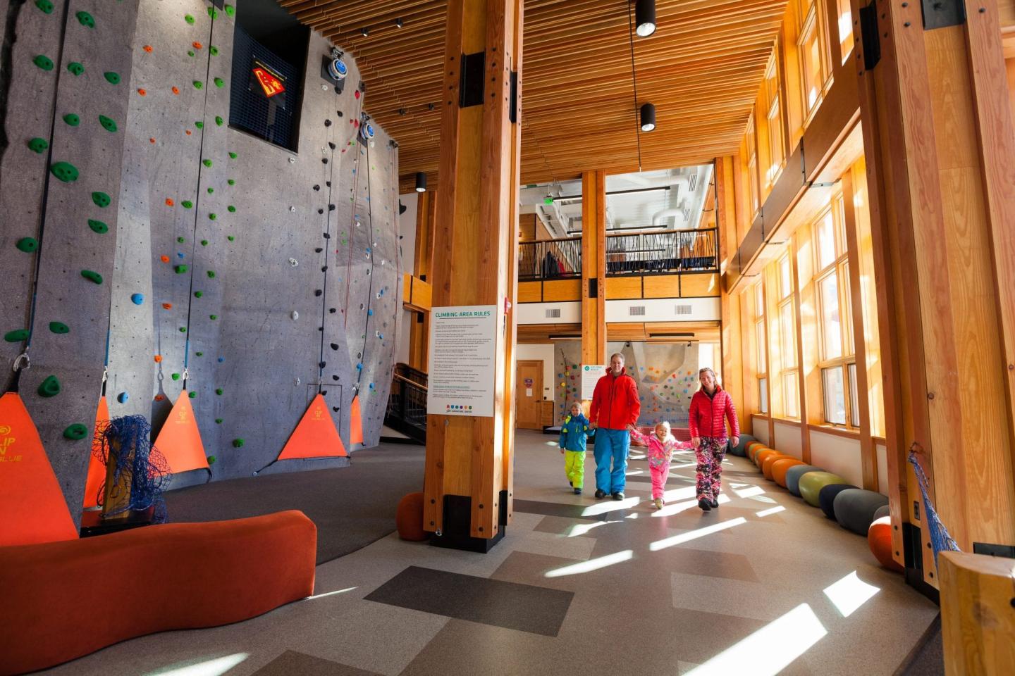 Indoor climbing gym with a family walking through, sunlight streaming in.