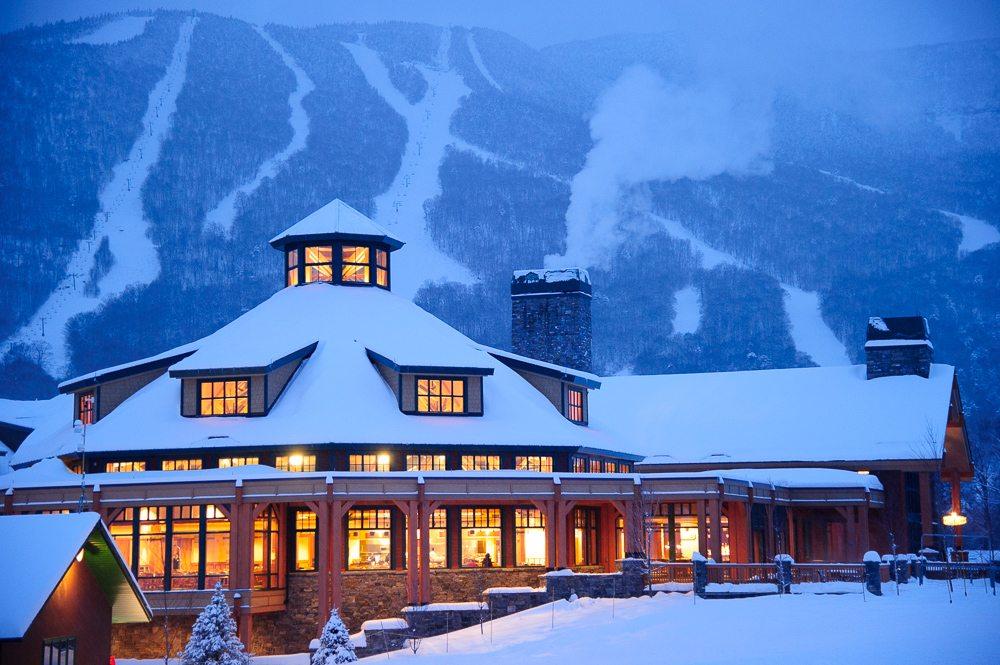 Snowy lodge lit warmly, mountains in the snowy background.