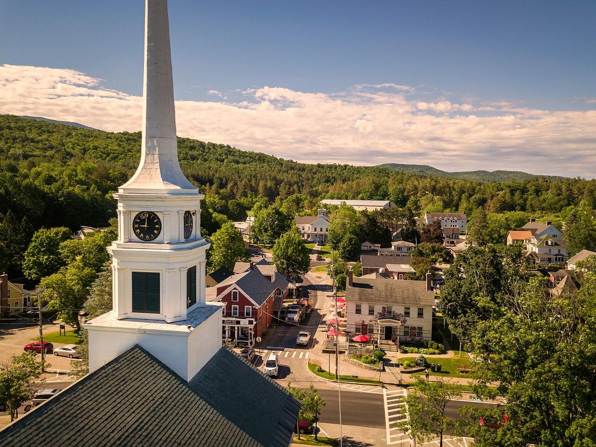 Town with a white church steeple, surrounded by trees under a blue sky.