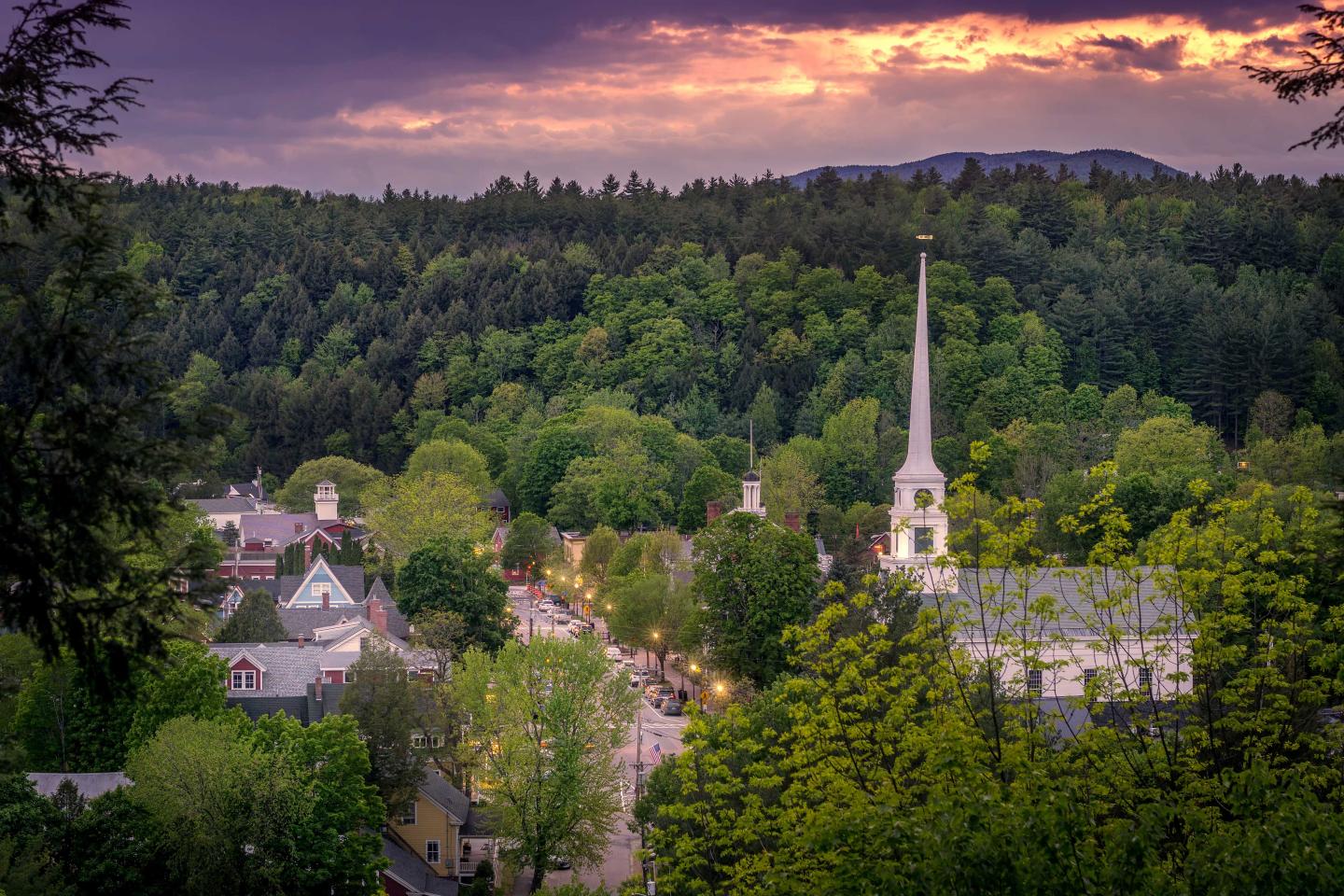 Town with white steeple, lush greenery, and a vibrant sunset sky.