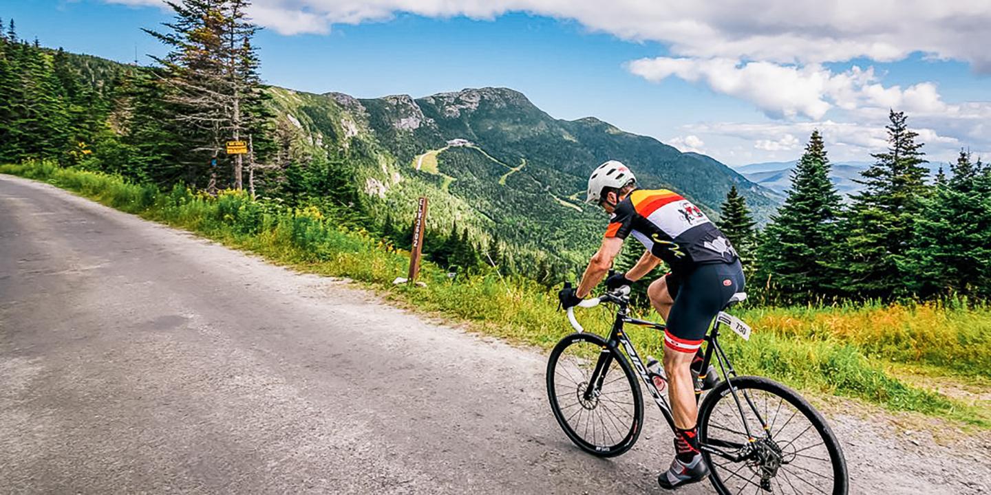 Cyclist on a mountain road, lush green scenery, under a partly cloudy sky.