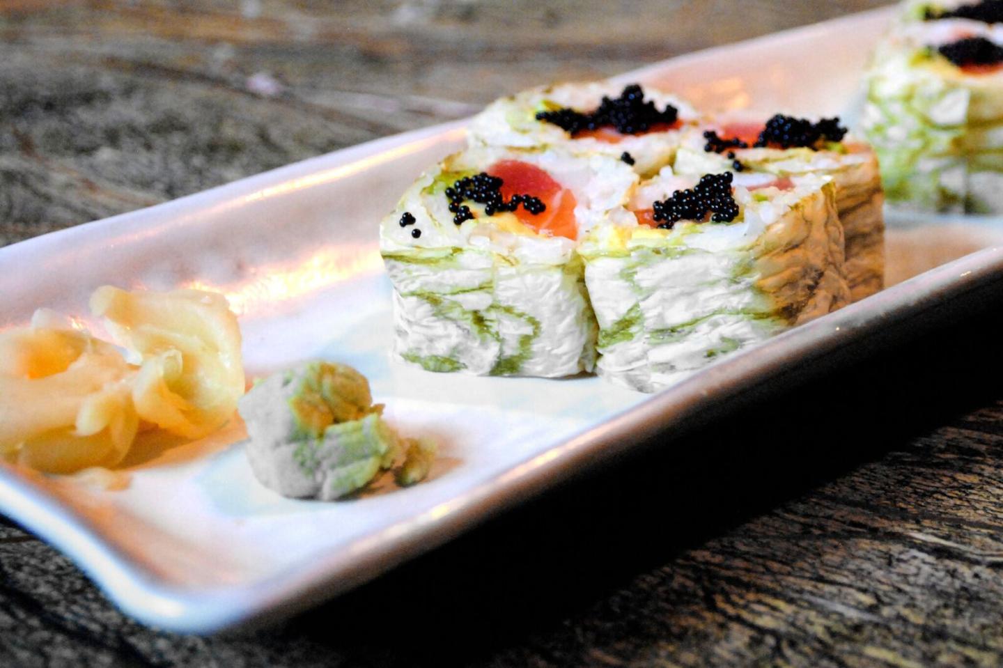 Sushi rolls on a white plate with wasabi and pickled ginger.