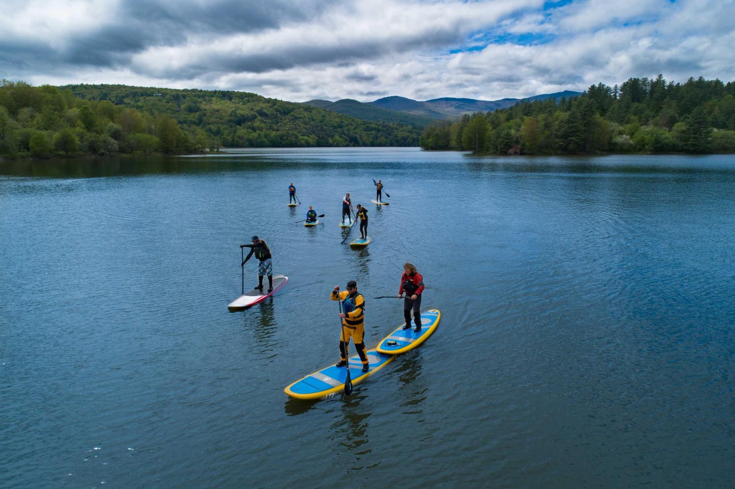 Paddleboarders on a calm lake surrounded by green hills under a cloudy sky.