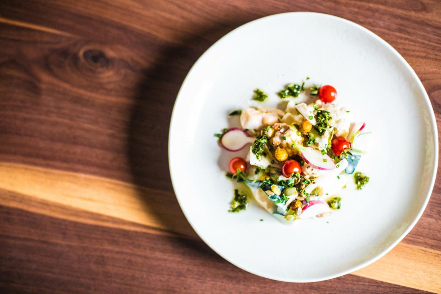 Colorful salad on a white plate, placed on a wooden table.