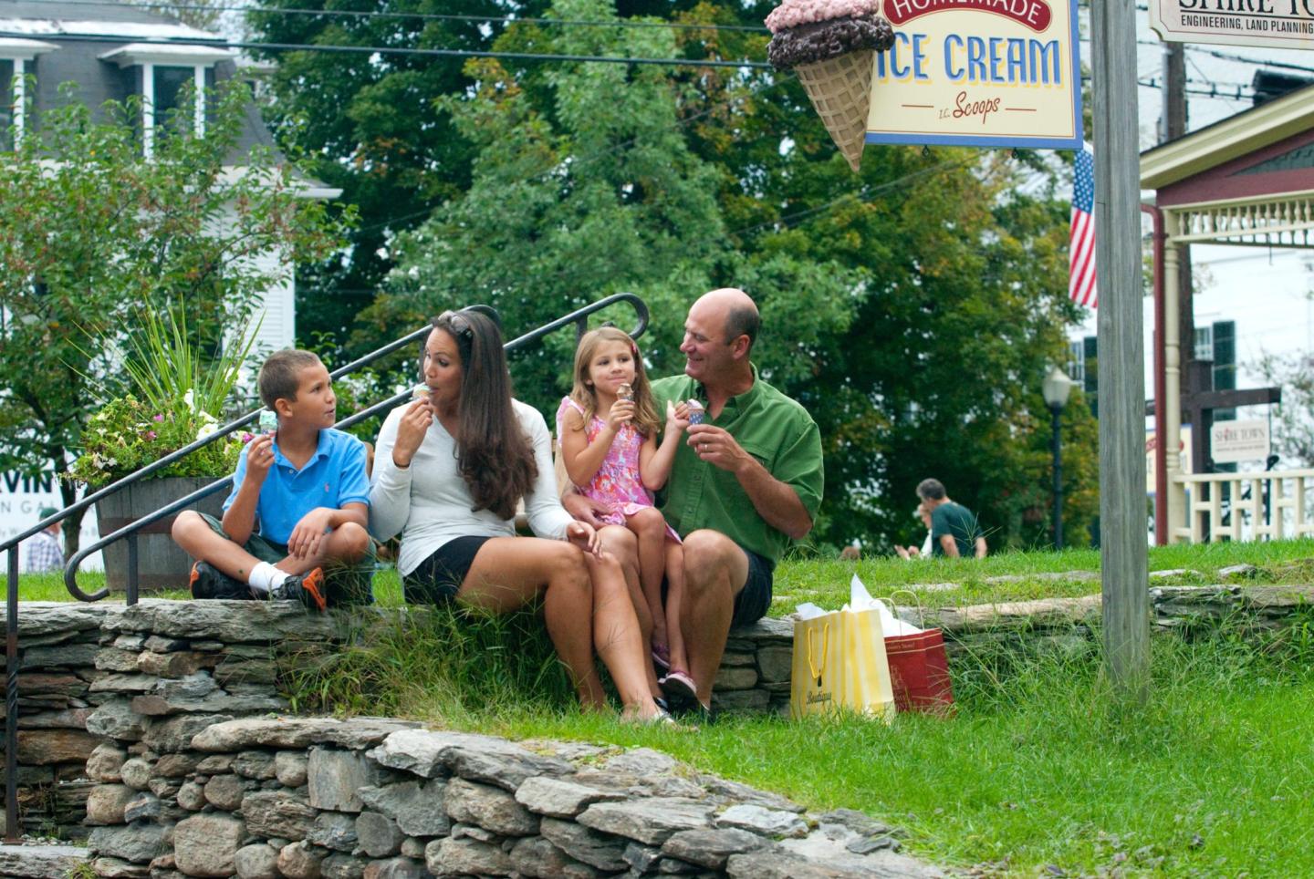 Family enjoying ice cream on a stone wall by a green lawn, ice cream shop sign visible.