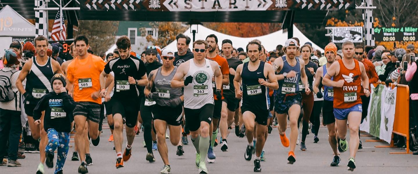Runners starting a race under a banner on an overcast day.