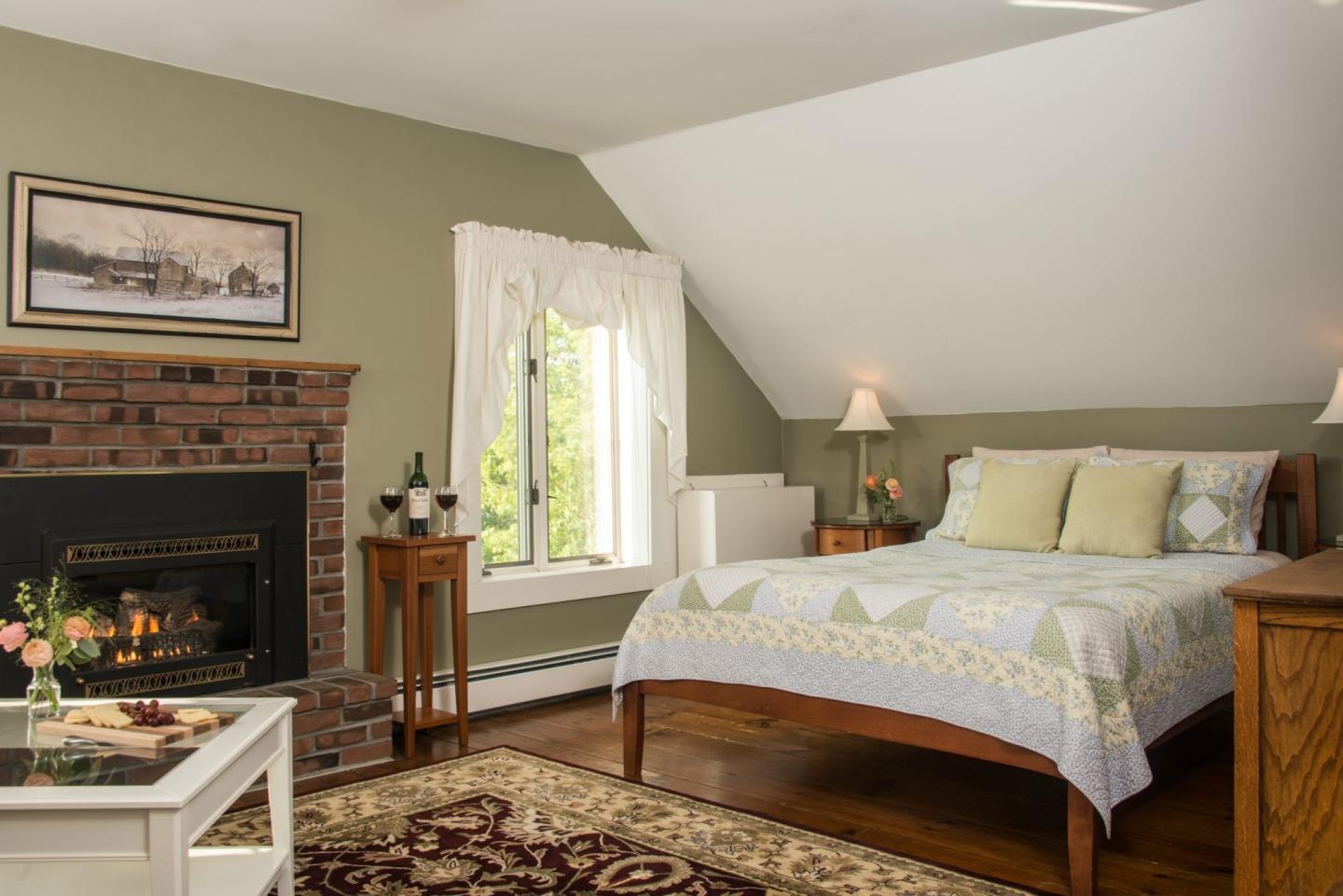 Cozy bedroom with a brick fireplace, bed, and window with drapes.
