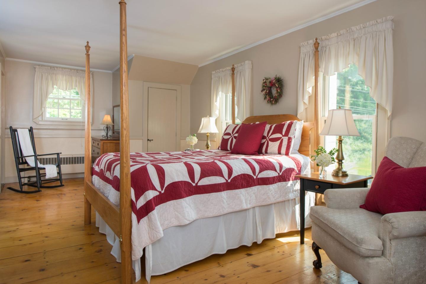 Cozy bedroom with a red and white quilt, wooden bed, and soft natural light through windows.