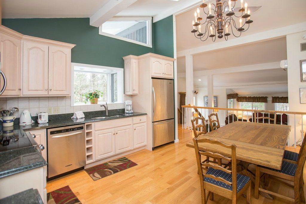 Spacious kitchen with wooden dining table, chandelier, and stainless steel appliances.