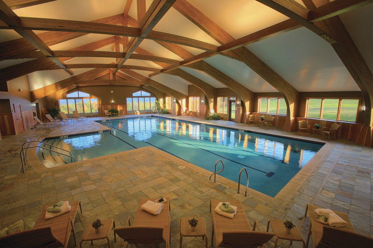 Indoor pool with wooden beams, lounge chairs, and large windows.