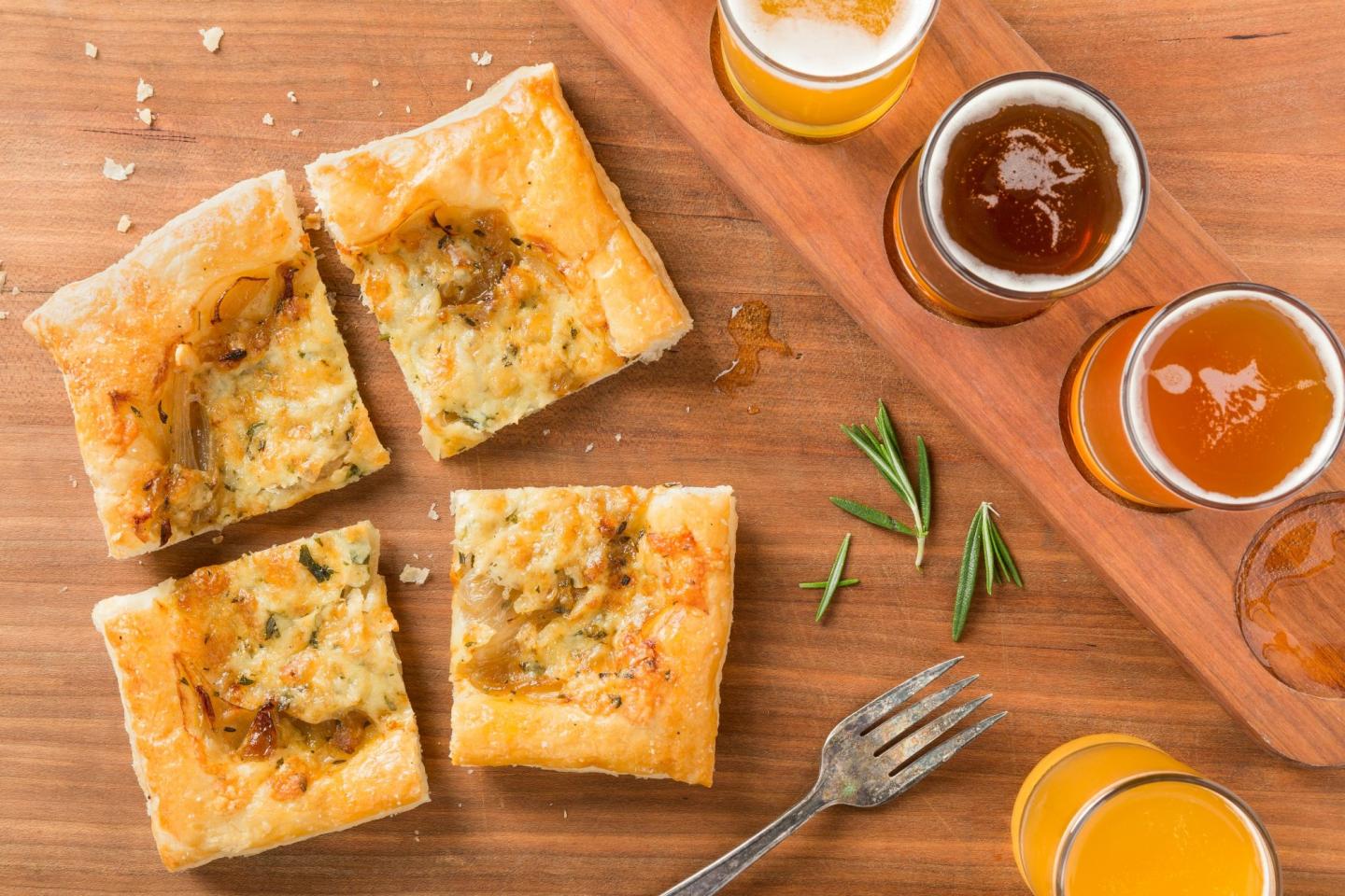 Pastries and four beer glasses on wooden board with rosemary sprigs.