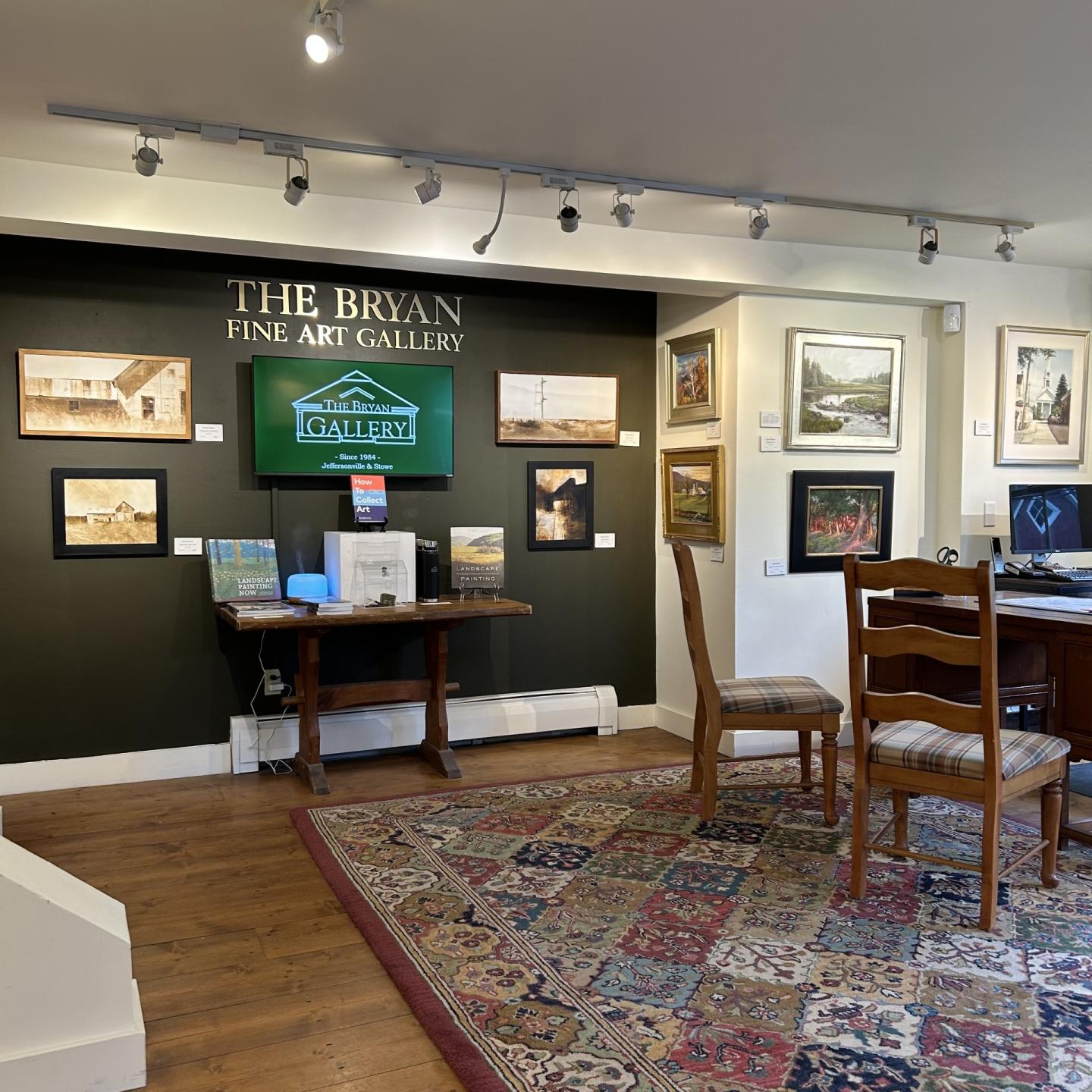 Art gallery with paintings on walls, wooden chairs, and a colorful rug.