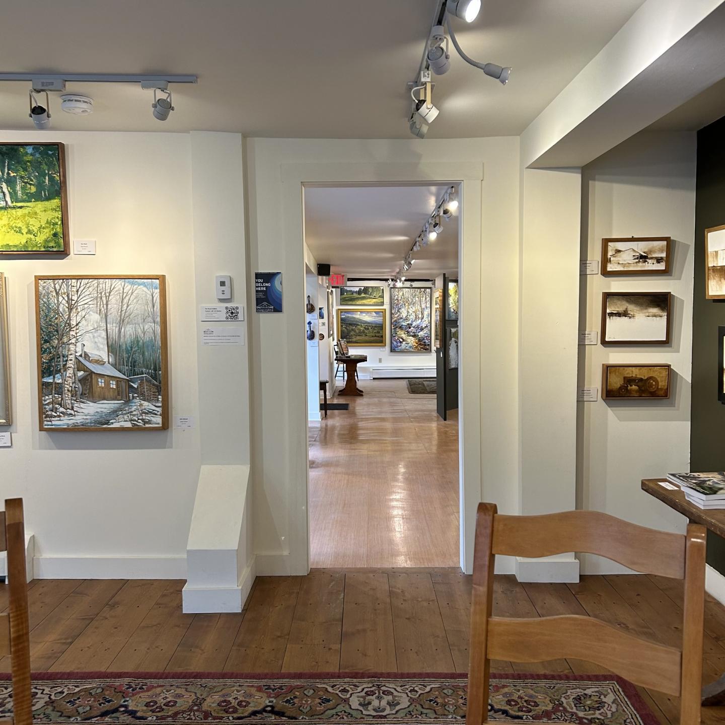 Art gallery interior with paintings on white walls and wooden floor.