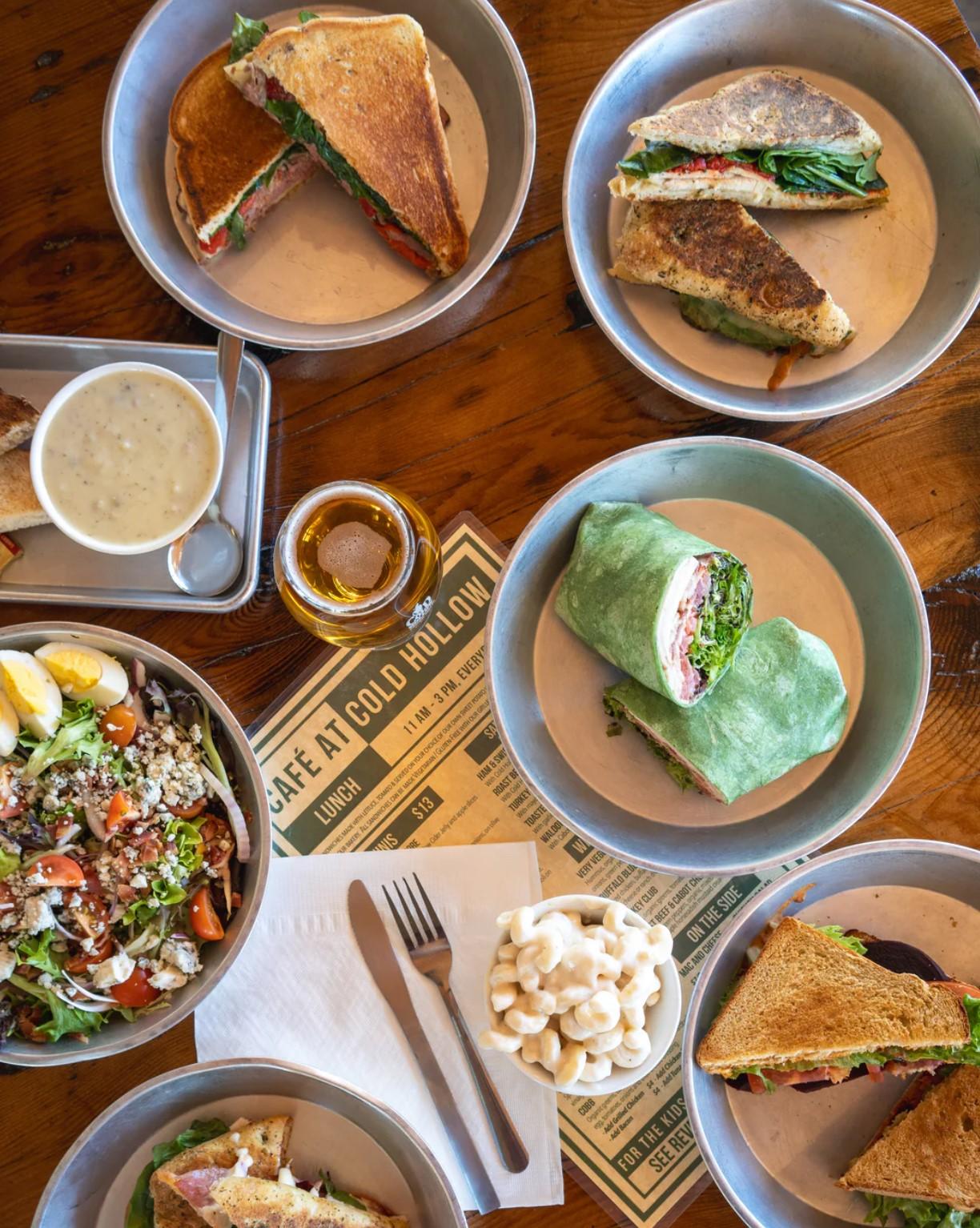 Plate of sandwiches, wraps, salad, and soup on a wooden table.