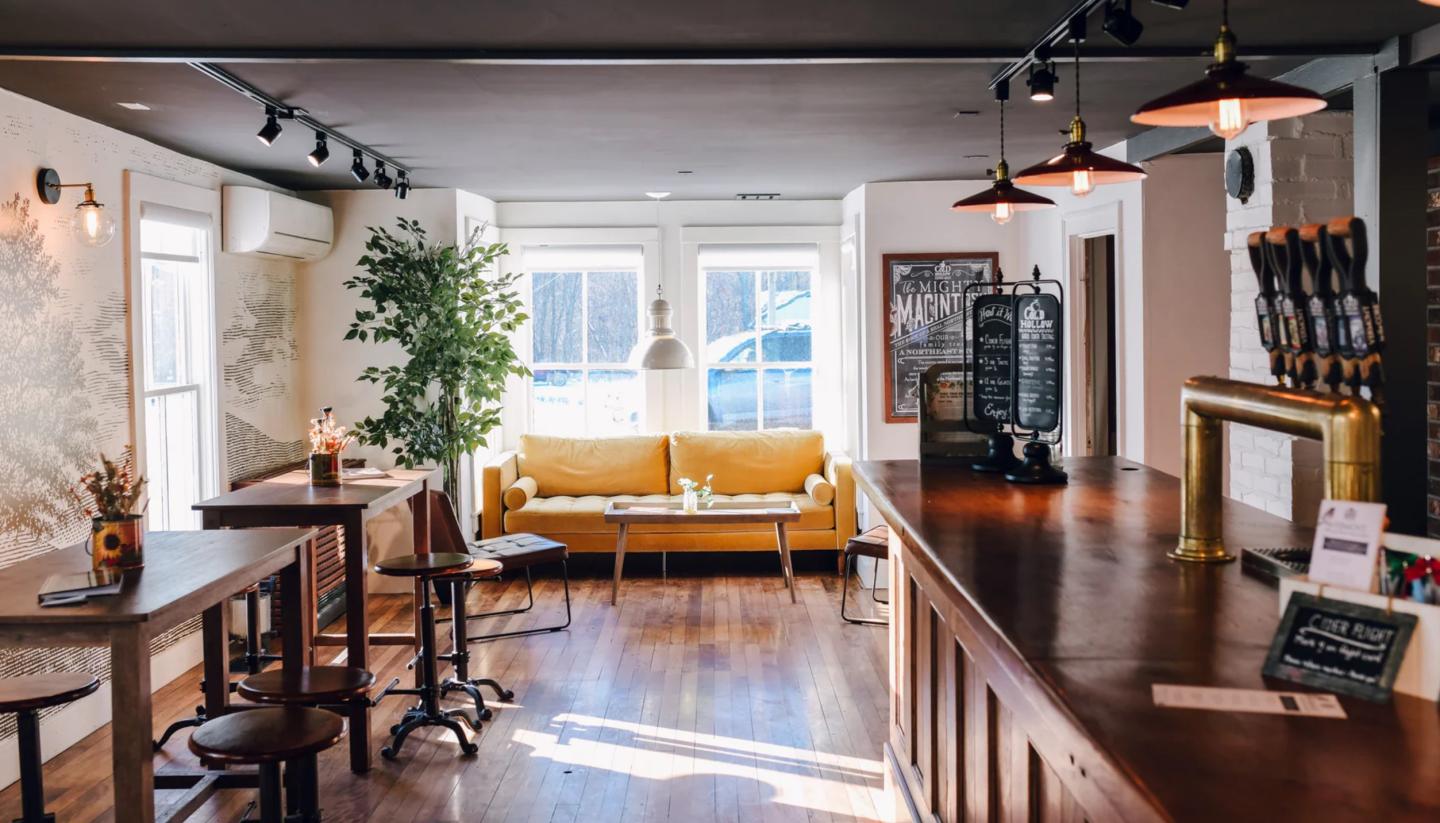 Cozy café with a yellow couch, wooden bar, and tables, lit by pendant lamps.