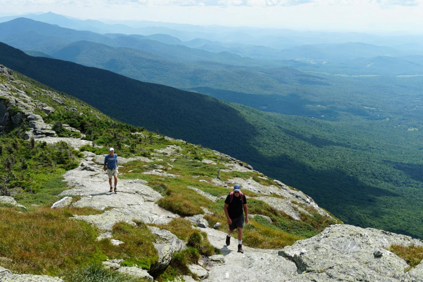 Hikers on a mountain trail with a vast valley view.