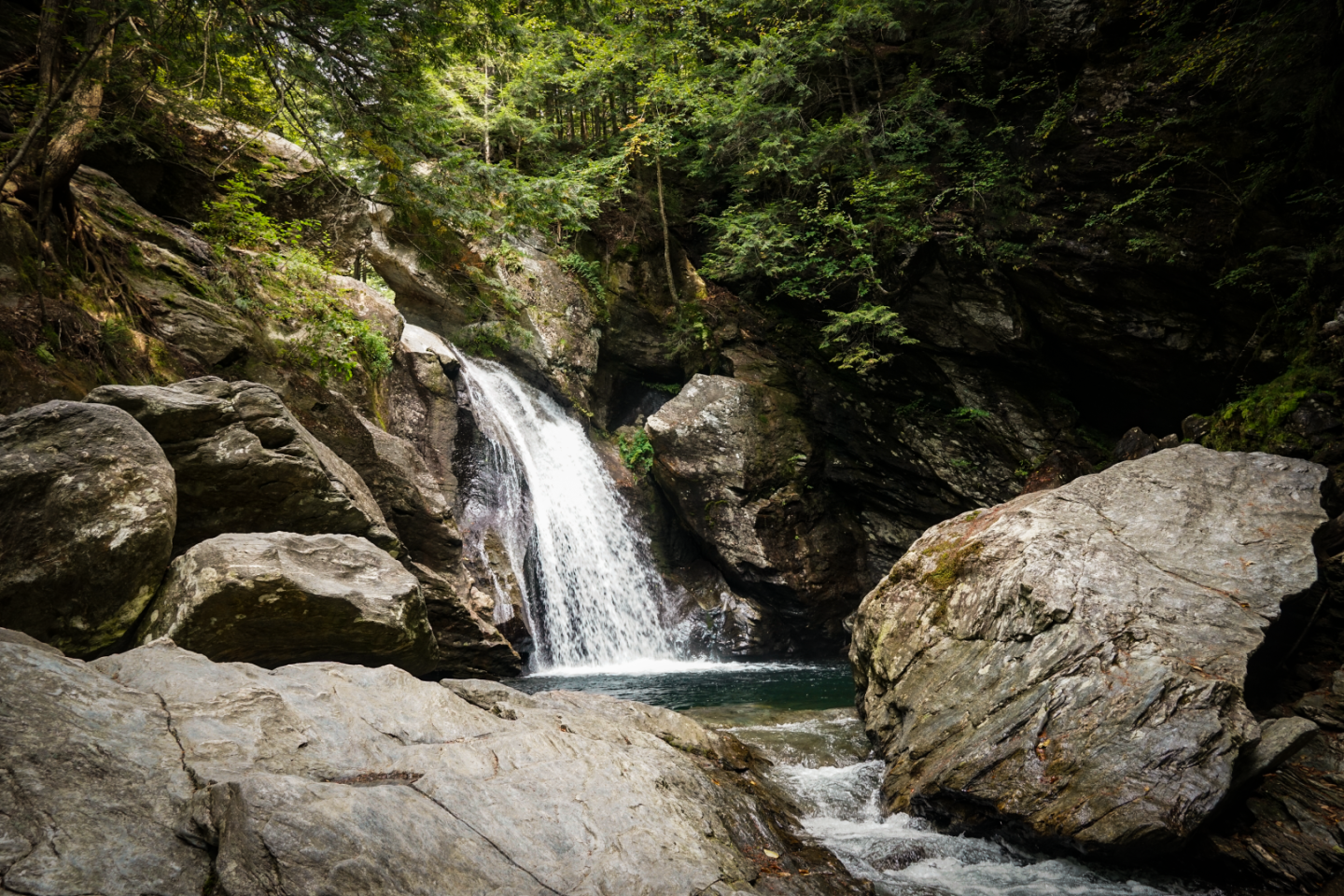 Waterfall flowing between rocks surrounded by lush green forest.