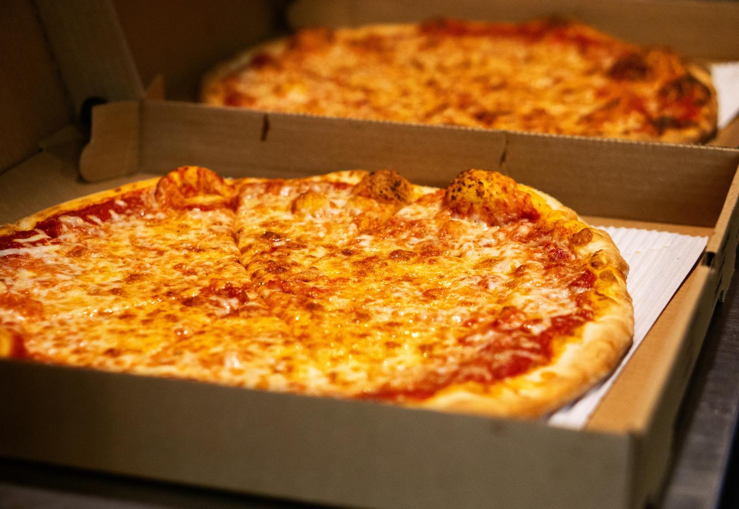 Two cheese pizzas in open cardboard boxes on a table.