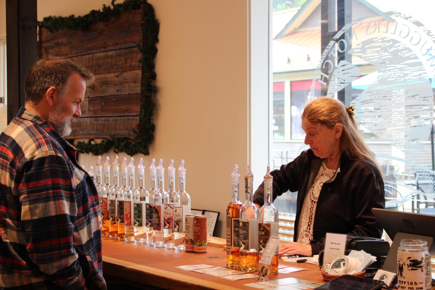Man at a tasting bar with bottles of spirits; woman serving drinks.