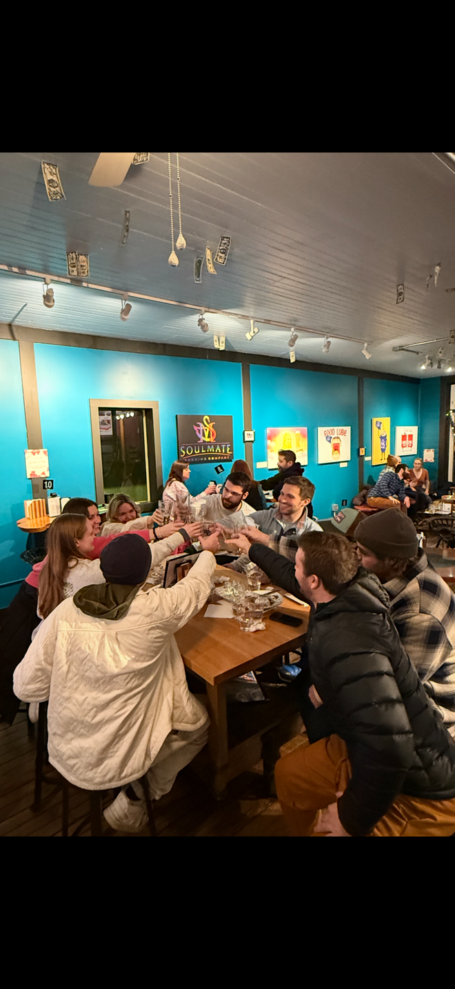 Group of people toasting at a wooden table in a vibrant, blue-walled cafe.