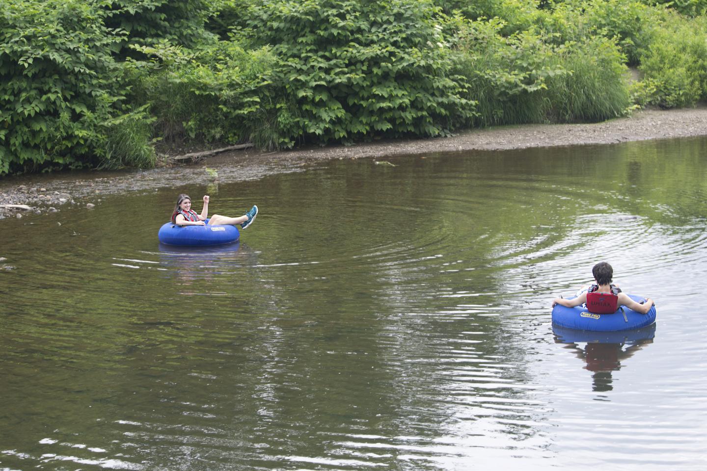 Two people tubing on a calm river surrounded by lush greenery.