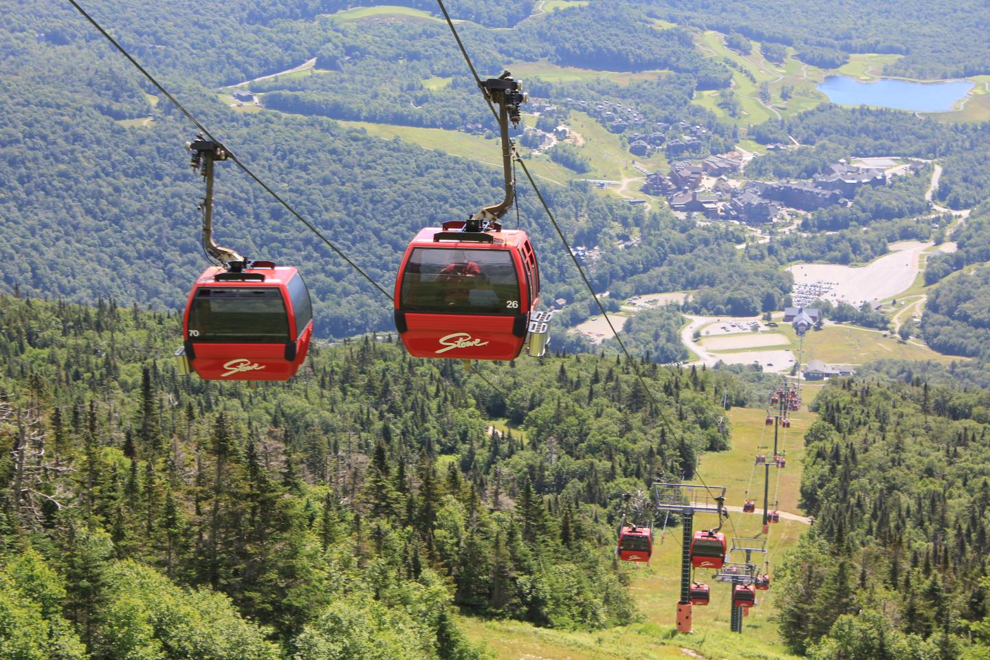 Red Gondola Cabins over a green mountain landscape on a sunny day.