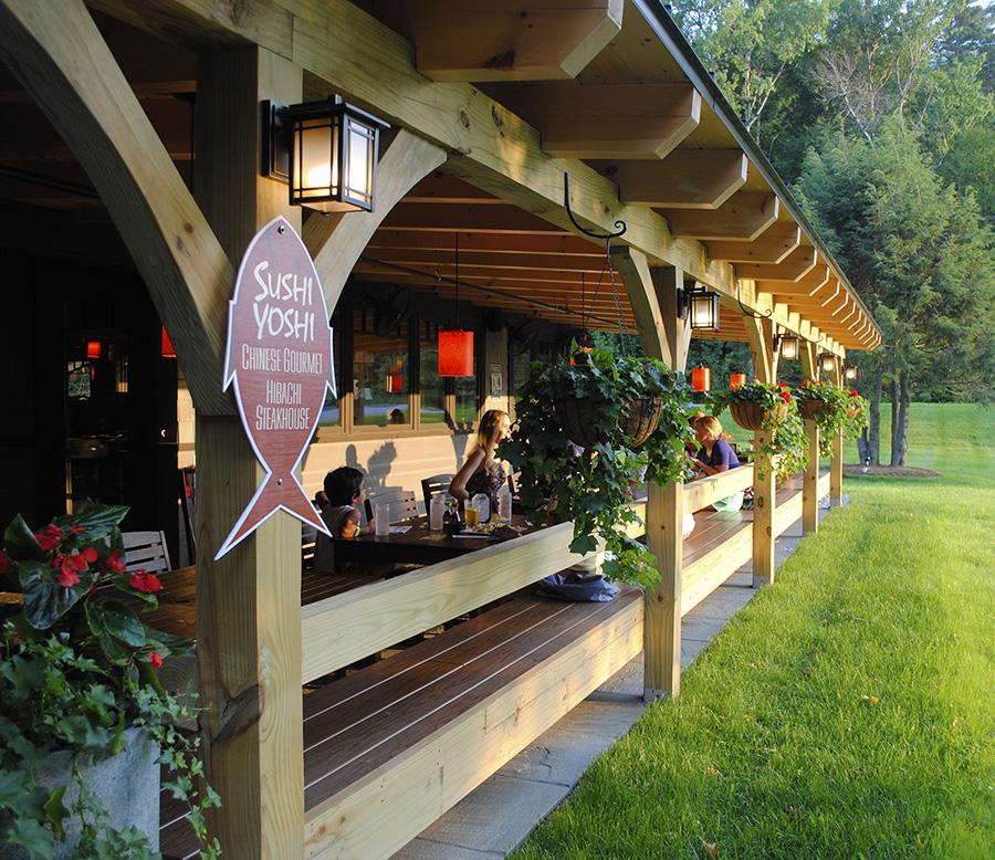 Wooden terrace with hanging plants, warm lighting, and greenery in the background.