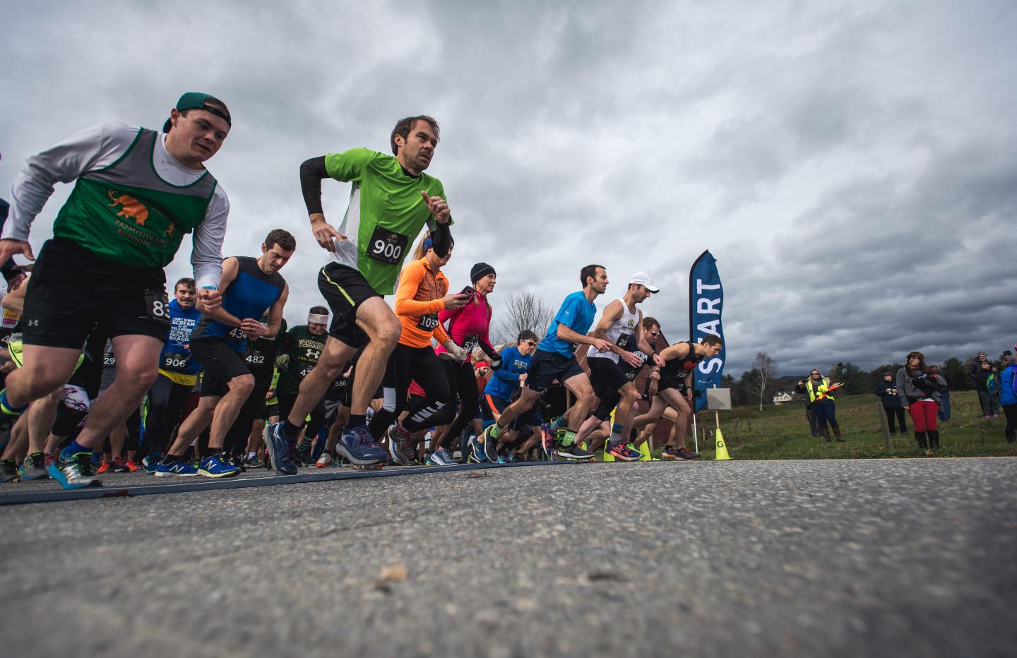 Runners starting a race, cloudy sky backdrop, varied sports attire.