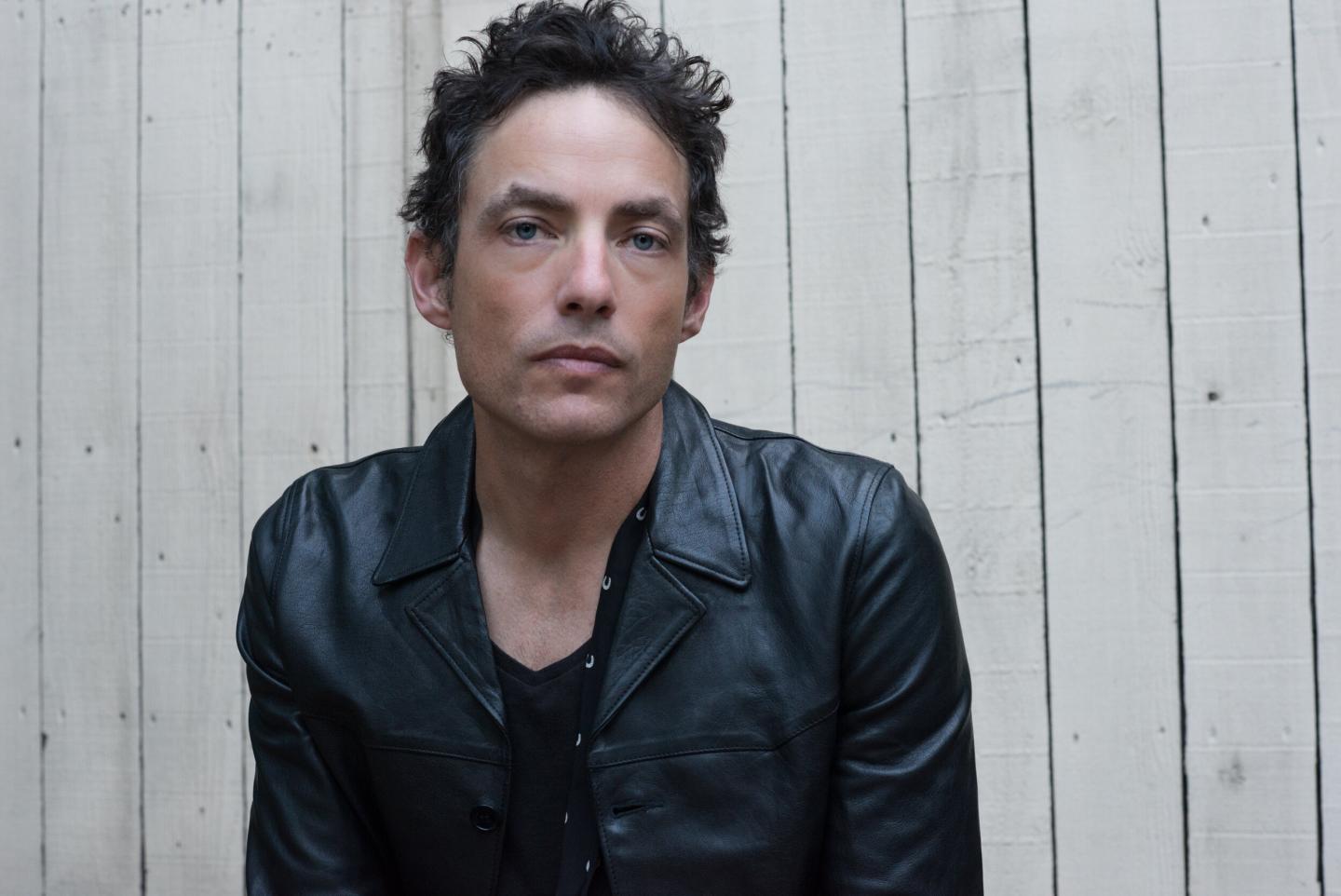 Man in black leather jacket against a wooden fence.