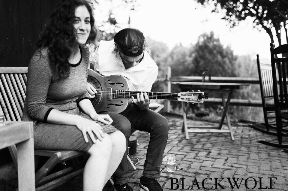 Man playing guitar next to smiling woman, outdoors, black and white photograph.