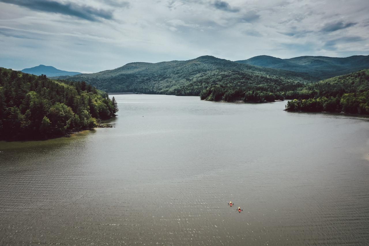 Calm lake with two kayaks, surrounded by green hills under a cloudy sky.