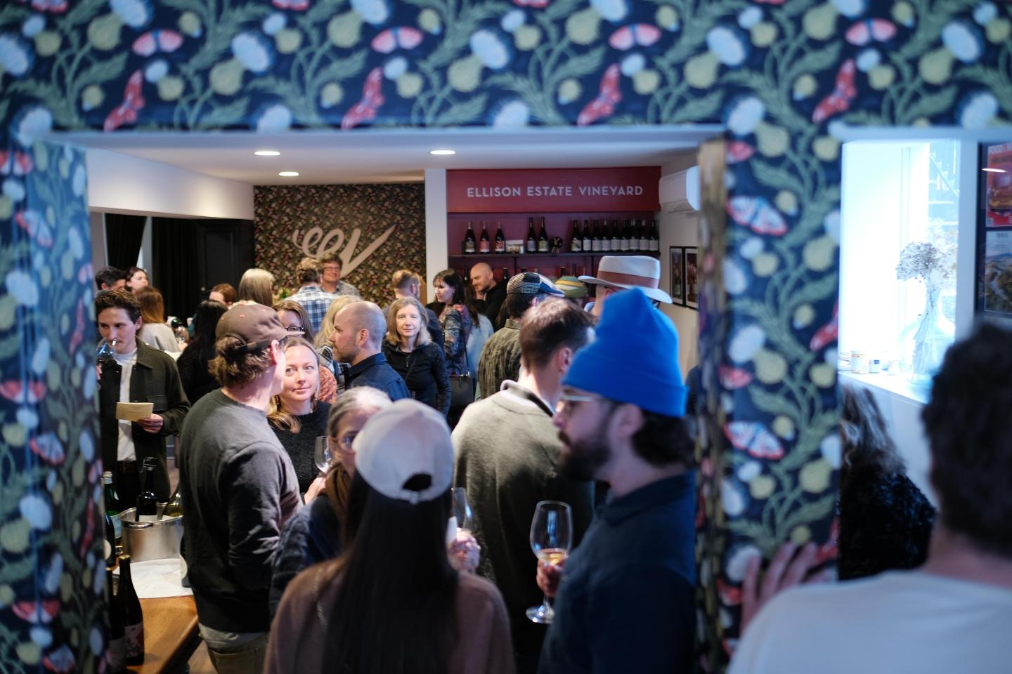 Crowded room with people socializing and a floral-patterned doorway.