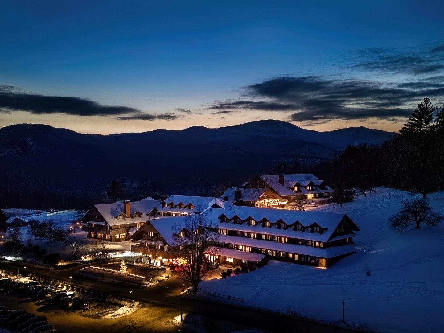 Snow-covered resort at dusk with mountains in the background.